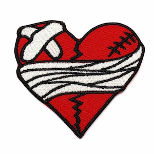 May include: A red heart-shaped embroidered patch featuring a black stitched crack down the center, a white adhesive bandage on the upper left, a white gauze wrap across the middle, and black stitches on the upper right side.