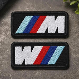 May include: Two rectangular embroidered patches featuring the letter M in white, followed by three diagonal stripes in red, dark blue, and light blue on a black background. One patch displays the M correctly, while the other shows a mirrored W.