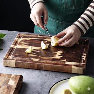 Puede incluir: Una tabla de cortar rectangular de madera con un patrón geométrico marrón oscuro y marrón claro. Una persona está cortando un limón en la tabla con un cuchillo. La tabla tiene una ranura para el jugo alrededor del borde.