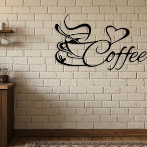 Könnte beinhalten: Eine weiße Keramik-Tasse mit schwarzem Henkel und dem Text "But First, Coffee" in schwarzer, handschriftlicher Schrift. Die Tasse steht auf einer weißen Oberfläche.