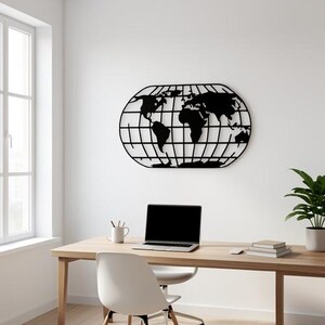 Op de afbeelding: Een zwarte metalen wereldkaart wanddecoratie in een ovale vorm, gemonteerd op een witte muur. De kaart bevindt zich boven een houten bureau met een laptop, mok en boeken. Een witte stoel staat voor het bureau.