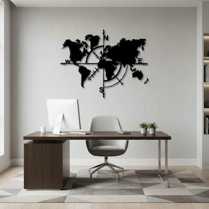 May include: Black metal world map wall art featuring a compass design. The map is mounted on a white wall above a desk. The desk has a computer monitor, a chair, and two small potted plants.