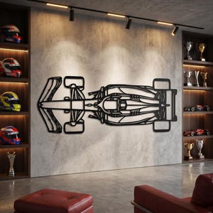 以下が含まれることがあります： 黒い金属製のF1レーシングカーの壁掛けアート。作品は、レーシングヘルメットとトロフィーが飾られた両側の棚がある、質感のある灰色の壁に取り付けられています。車のデザインは上から見え、その空力的な形状を示しています。