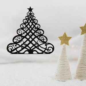 Op de afbeelding: Zwarte metalen kerstboomdecoratie met een ster. De boom heeft een ingewikkeld, open ontwerp. Twee kleine, met wit touw omwikkelde kegelvormige bomen zijn bekroond met gouden glittersterren.