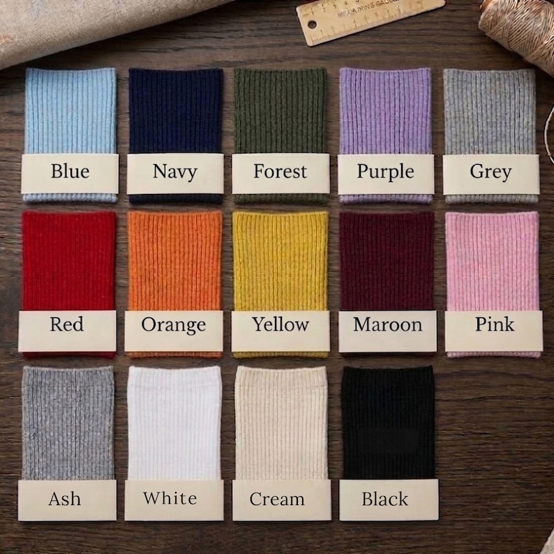 May include: A collection of ribbed fabric swatches in various colors, including blue, navy, forest green, purple, grey, red, orange, yellow, maroon, pink, ash, white, cream, and black. Each swatch has a label with its color name.