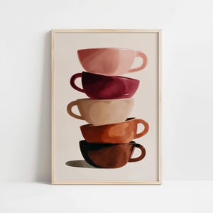 May include: A framed art print featuring a stack of five coffee cups in shades of pink, burgundy, beige, orange, and brown. The cups are stacked vertically, with a light beige background and a shadow beneath the bottom cup.