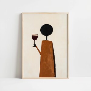 May include: A framed wall art print featuring a stylized figure with a solid black circular head and a brown rectangular body. The figure holds a stemmed glass containing a dark red liquid. The background is a solid, light cream color.