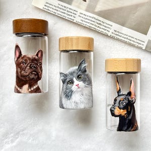 May include: Three glass bottles with wooden lids, each featuring a painted pet portrait. One bottle has a brown French Bulldog, another a gray and white cat, and the last a black and tan Doberman.