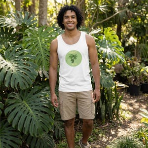 May include: A white tank top with a green and white graphic that says "Plant Papi." The tank top is worn with khaki cargo shorts. The person is standing in a lush green garden.