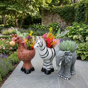 以下が含まれることがあります： キリン、シマウマ、ゾウの形をした3つのプランター。キリンは茶色で模様入り、シマウマは白と黒の縞模様、ゾウはグレーです。各プランターには、庭の装飾に最適な、カラフルな花と緑が入っています。