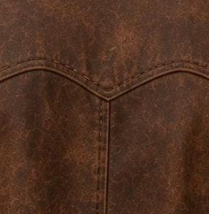 May include: Close-up of a brown leather jacket's back yoke and stitching. The leather has a distressed, textured appearance with variations in colour. The stitching is visible and follows the curved design of the yoke.