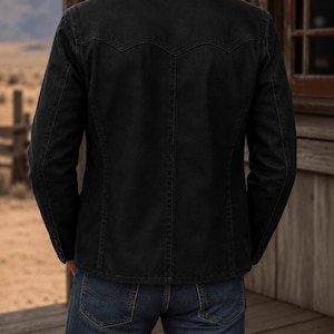 May include: A black denim jacket featuring a pointed western-style back yoke, a fold-down collar, and long sleeves with buttoned cuffs, paired with dark blue denim jeans. The jacket has visible vertical seam detailing and a structured fit.