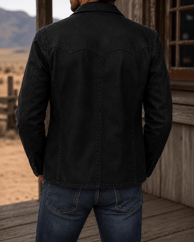 May include: A black denim jacket featuring a pointed western-style back yoke, a fold-down collar, and long sleeves with buttoned cuffs, paired with dark blue denim jeans. The jacket has visible vertical seam detailing and a structured fit.