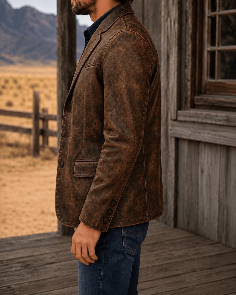 May include: A brown leather blazer with a distressed effect. The jacket features a notched lapel, a single-breasted design, and three buttons on the sleeve. It is worn with blue denim jeans.