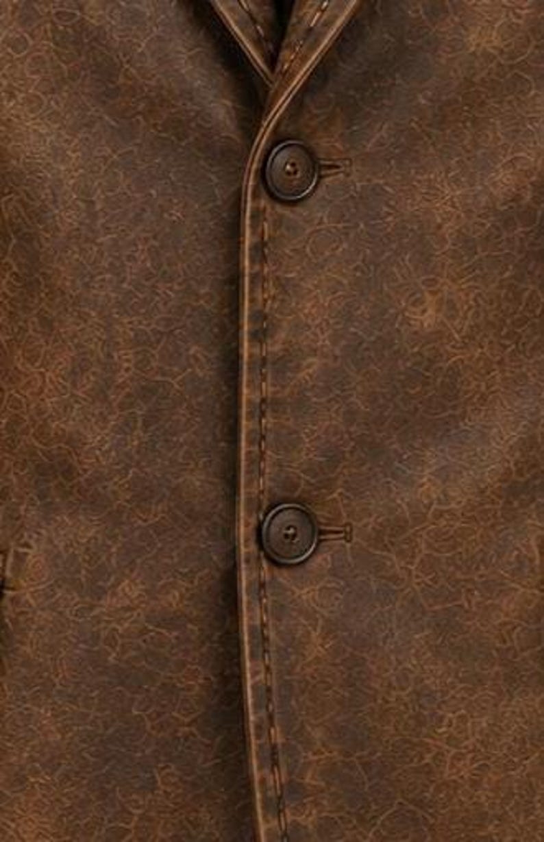 May include: Close-up of a brown leather blazer with two dark brown buttons. The blazer has a textured surface and visible stitching along the seams. The jacket's colour is a rich, warm brown.