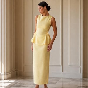 May include: A pale yellow sleeveless dress featuring a fitted bodice with a peplum waist and side lace-up detailing. The skirt is floor-length and straight, crafted from a textured fabric. The garment has a round neckline and a clean, structured silhouette.