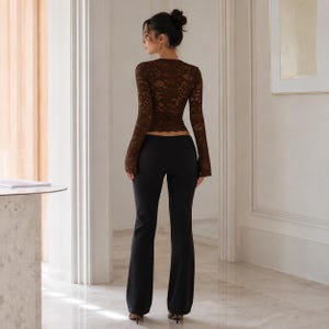 May include: A long-sleeved brown lace top with a scalloped hem paired with solid black flared trousers. The top features a fitted silhouette with intricate floral lace patterns, while the trousers have a smooth finish and a full-length cut.