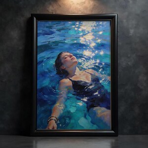 May include: A framed oil painting depicts a person floating in blue water, eyes closed, wearing a black swimsuit. The water reflects sunlight, creating bright spots. The artwork is framed in a black rectangular frame.