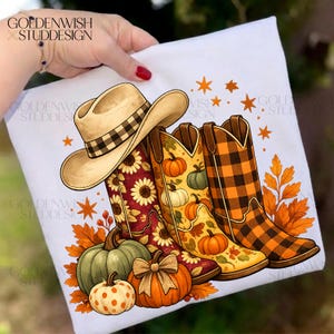 Puede incluir: Una camiseta blanca con un estampado gráfico de un sombrero de vaquero color canela, tres botas de estilo western y varias calabazas. Las botas muestran patrones de girasoles, calabazas y cuadros. Hojas de otoño naranjas y estrellas rodean los elementos.