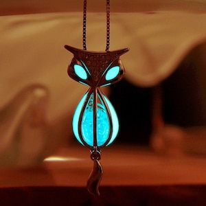 Puede incluir: Un collar de plata con un colgante de gato azul brillante. El gato tiene una cola larga y está hecho de metal con un cuerpo de vidrio transparente.