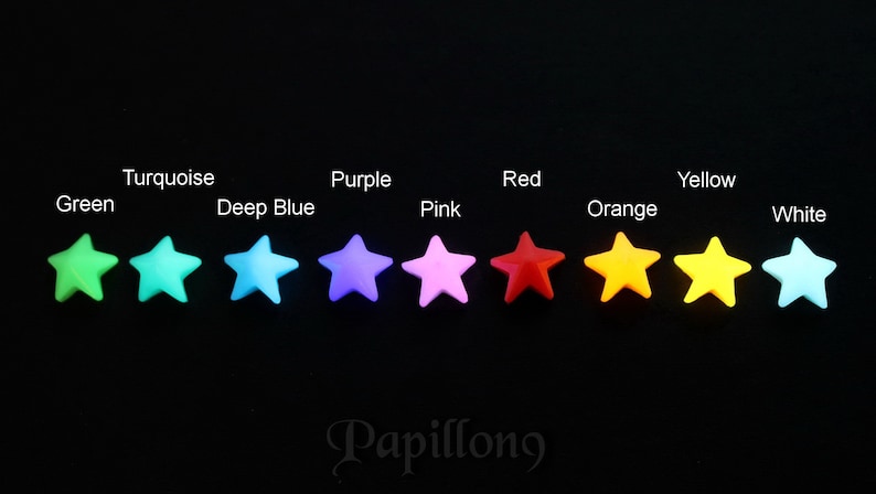 May include: A collection of colorful star-shaped embellishments in green, turquoise, deep blue, purple, pink, red, orange, yellow, and white. The stars are arranged in a row against a black background, with the word "Papillong" in the bottom right corner.