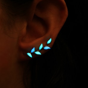 May include: A pair of glow-in-the-dark ear cuffs shaped like a branch with leaves. The leaves are a light blue and green color.