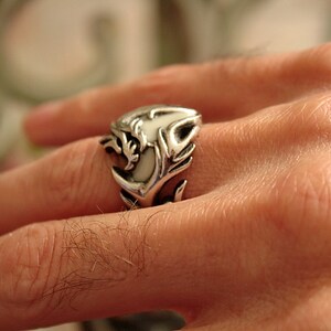 Peut inclure: Une bague en argent avec un motif de dragon blanc. La bague est port&eacute;e au doigt d'une personne.