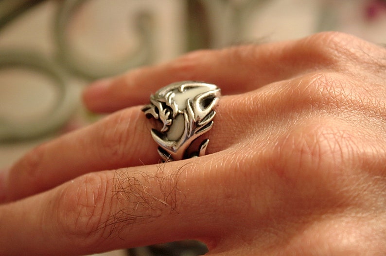 Peut inclure: Une bague en argent avec un motif de dragon blanc. La bague est port&eacute;e au doigt d'une personne.
