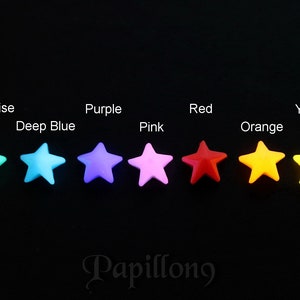 Peut inclure: Une rang&eacute;e de dix boutons en forme d'&eacute;toile de diff&eacute;rentes couleurs, notamment vert, turquoise, bleu fonc&eacute;, violet, rose, rouge, orange, jaune, blanc et noir. Les boutons sont dispos&eacute;s en ligne de gauche &agrave; droite, les couleurs passant progressivement du vert au noir.