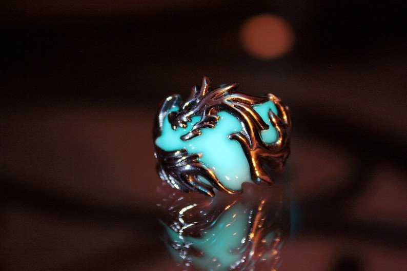 Peut inclure: Une bague en argent avec un motif de dragon vert brillant. Le dragon est enroul&eacute; autour d'une pierre verte.