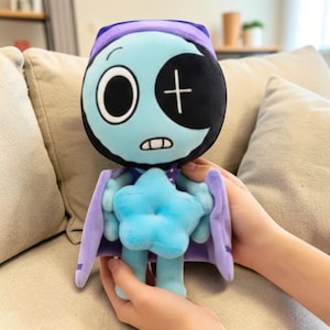 May include: A plush toy featuring a cartoon character with a light blue crescent moon face, a black eye patch with a white cross, and a purple hat. The character holds a light blue star and has purple wings.