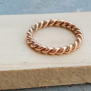 May include: A copper-coloured ring with a twisted rope design. The ring is circular and appears to be made of metal. The ring is on a light-coloured surface.