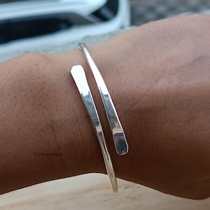 Op de afbeelding: Een zilverkleurige manchetarmband met een open ontwerp. De armband heeft een gehamerde textuur en wordt om een pols gedragen. De tekst "925Shreejaipur" is zichtbaar op de pols.