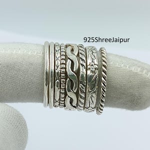 Pode incluir: Uma coleção de anéis de prata com vários designs, incluindo padrões trançados, florais e texturizados. Os anéis são empilhados, mostrando diferentes larguras e estilos. O texto "925Shreejaipur" é visível.