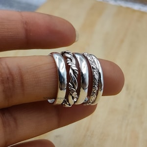 Könnte beinhalten: Ein Set aus vier Silberringen mit unterschiedlichen Designs, darunter zwei glatte Bänder, ein gedrehtes Seil-Design und ein Band mit einem komplizierten geätzten Muster. Der Text 925ShreeJaipur ist auf der Oberfläche des glatten Rings sichtbar.