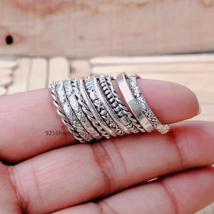 Peut inclure: Plusieurs bagues en argent avec divers motifs texturés, tressés, à motifs et lisses. Les bagues sont empilées sur un doigt, présentant les différents styles. Le texte "925Shreelajpur" est visible.