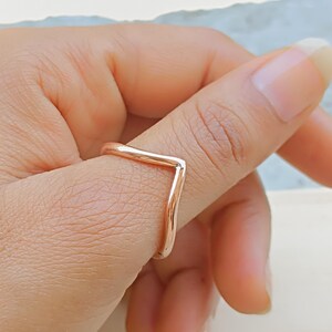 Op de afbeelding: Een roségouden V-vormige ring. De ring heeft een minimalistisch ontwerp met een gladde, gepolijste afwerking. De ring wordt om een vinger gedragen en toont zijn elegante, moderne stijl. De kleur van de ring is een warme, metallic tint.