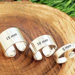 Könnte beinhalten: Drei silberfarbene, offene Ringe mit glatten, polierten Oberflächen. Die Ringe sind mit Text beschriftet, der Breiten von 15 mm, 10 mm bzw. 5 mm angibt. Jeder Ring weist eine Lücke im Band auf, die eine verstellbare Passform am Finger ermöglicht.