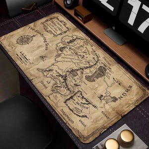 May include: A rectangular desk mat in tan, depicting a detailed map of Middle-earth. The map includes geographical features, place names, and a compass rose. The mat has a vintage, aged appearance, with text that reads "A Mappe of Middle-Earth" and "The Sundering Seas".