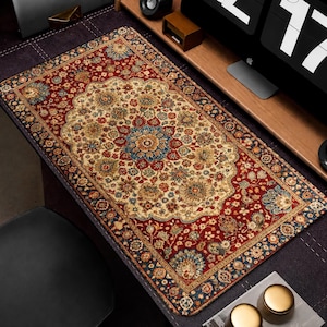May include: A rectangular desk mat with a Persian rug design. The mat features a central cream-colored medallion with floral patterns in red, blue, and gold, framed by a deep red border with similar floral motifs. The mat measures approximately 31 inches long and 16 inches wide.