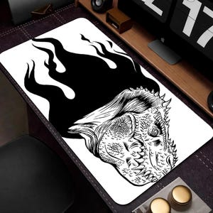 May include: A rectangular desk mat featuring a high-contrast black and white graphic illustration of a dinosaur head. The dinosaur is depicted with sharp teeth and textured scales, with a large, solid black flame-like shape rising behind it.