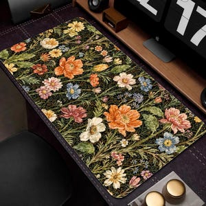 Puede incluir: Una alfombrilla de escritorio rectangular con un dise&ntilde;o floral que presenta flores naranjas, rosas, amarillas y azules sobre un fondo oscuro. La alfombrilla tiene un borde cosido y est&aacute; dise&ntilde;ada para una configuraci&oacute;n inform&aacute;tica.