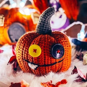 May include: A handcrafted orange crochet pumpkin with a grey stem, yellow and black button eyes, and a stitched smile with a single white tooth. A festive Halloween decoration.