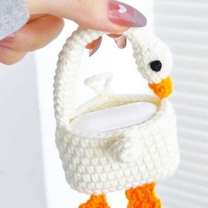 May include: A handmade, white crochet goose-shaped soap holder with orange feet and beak. The goose has a black eye and is holding a white bar of soap. The handle is also white.