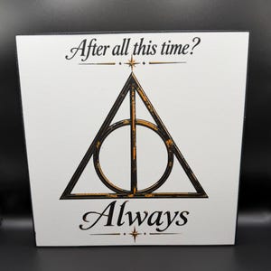May include: A square white sign featuring a black and gold distressed Deathly Hallows symbol in the center. The text "After all this time?" is printed in black above the symbol, and the word "Always" is printed in black below the symbol.
