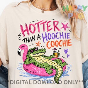 May include: Cream-colored t-shirt with a colorful graphic. The graphic features an alligator in sunglasses relaxing on a pink flamingo float, holding a drink. Text reads "HOTTER THAN A HOOCHIE COOCHIE."
