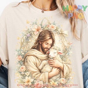 Könnte beinhalten: Cremefarbenes T-Shirt mit einer Aquarellillustration von Jesus, der ein Lamm umarmt, umgeben von einem Blumenkranz. Das Design verwendet sanfte Pastellfarben und enthält den Text "***DIGITAL DOWNLOAD ONLY***".