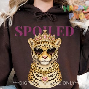 Op de afbeelding: Een bruine hoodie met een luipaard met een zonnebril, een kroon en een gouden ketting. Het woord "SPOILED" is in het paars gedrukt. Het ontwerp is een digitale afbeelding.