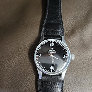 May include: A black-faced Rolex Marconi wristwatch with a silver case and a black leather band. The watch face features white numerals at the 12, 9, and 6 o'clock positions. The watch band has a gold-colored buckle.