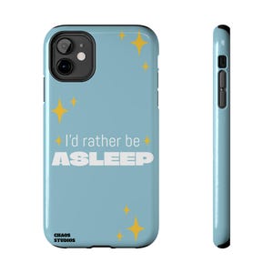 Peut inclure: Coque de téléphone bleu clair avec le texte "I'd rather be ASLEEP" en blanc. L'étui présente des graphiques d'étoiles jaunes et le logo "CHAOS STUDIOS". L'étui est conçu pour un smartphone.